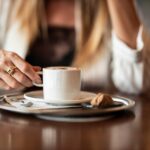 Una tazza di caffè su un tavolo, con un piatto vuoto di pranzo accanto.